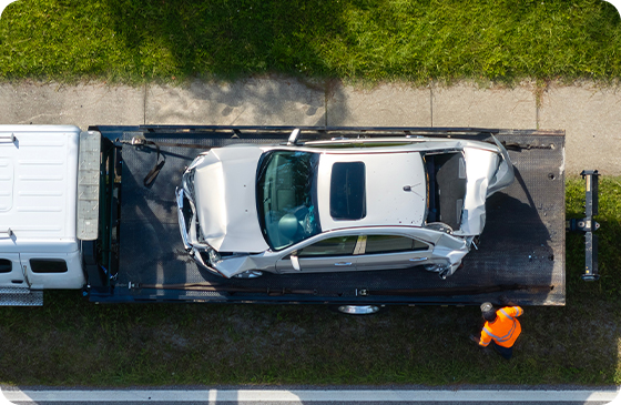 A damaged car on a rollback with an operator in high visibility orange