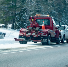 Government towing incident in action with police and tow truck driver working together to tow a vehicle off the side of a snowy road