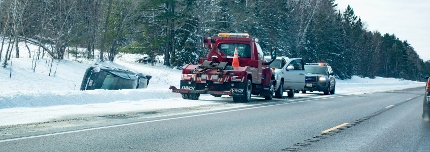 Government towing incident in action with police and tow truck driver working together to tow a vehicle off the side of a snowy road